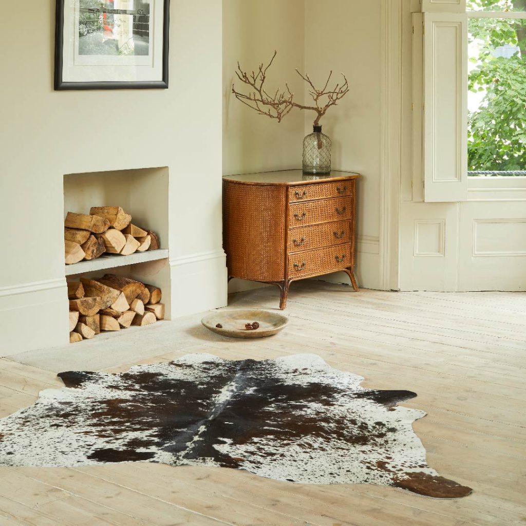 natural cowhide laid out on a wooden floor infront of a log store and oak chest of drawers.